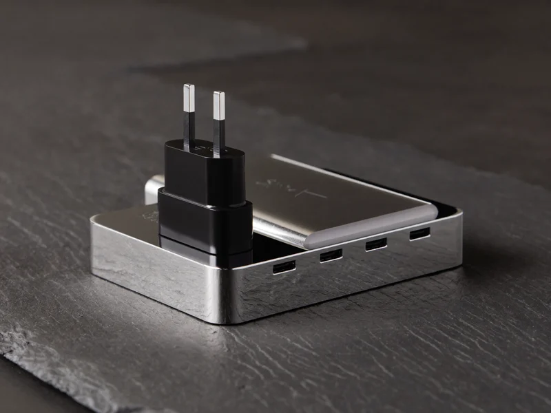 Kompakter Aluminium-USB-Hub neben einem Reiseadapter auf Schiefer